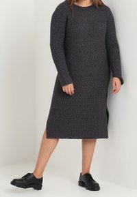 Ribbed long-sleeve sweater dress in dark gray, featuring a round neckline and side slits, paired with black lace-up shoes.