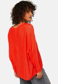 Rotes, langärmliges Strickoberteil mit lockerer Passform, V-Ausschnitt und Fledermausärmeln. Weicher Stoff mit leicht durchsichtiger Optik.