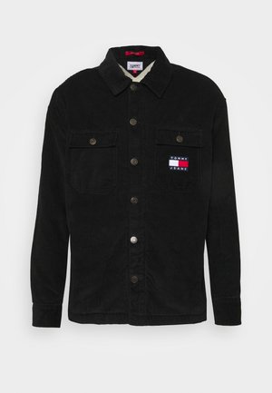 Veste noire en velours côtelé à boutons avec col, deux poches poitrine à rabat et écusson Tommy Jeans sur la poche droite.