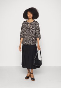 Blusa estampada em preto e bege com mangas três quartos, combinada com uma saia plissada preta. Acessórios incluem uma pequena mala preta.