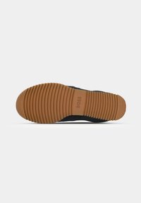 Fekete sneaker, texturált felsőrésszel és bordázott gumitalppal, amelyen jól látható a márkájának logója.