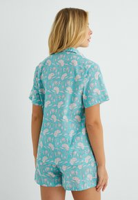 Conjunto de pijama de manga corta en color turquesa con estampados florales en blanco y rosa. Presenta un cuello y pantalones cortos de corte relajado con una cintura elástica.