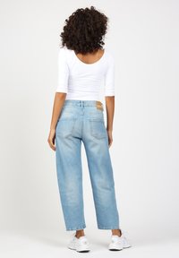 Light blue straight-leg jeans with a mid-rise fit, featuring a tan leather logo patch, two back pockets, and a clean hem. Paired with a white top.