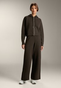 Hanorac tricotat maro cu un design scurt, închidere cu fermoar și șnururi, asociat cu o pereche de pantaloni larghi asortați. Material texturat, confortabil.