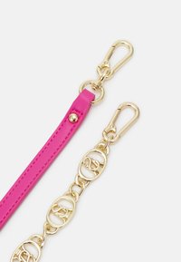 Chaîne en métal doré et bandoulière en cuir rose avec fermoirs dorés sur fond blanc, partie d’un accessoire de sac à main.