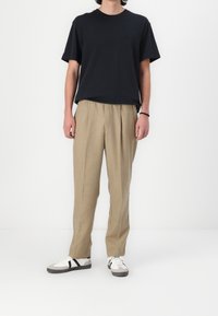 Sort T-shirt med korte ærmer, beige plisserede bukser og hvide sneakers med sorte detaljer. Enkel, afslappet pasform. Glat bomuld og struktureret stof.