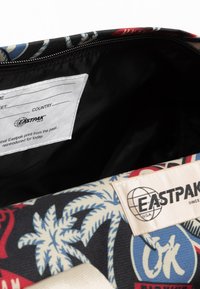 Eastpak-repun sisäpuoli, jossa musta vuori, värikäs palmupuusumu kankaalla, valkoinen etiketti brändin logolla ja rekisteröintilappu.