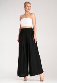 Czarne spodnie szerokie z luźnym krojem, wyposażone w wysoki elastyczny pas. W komplecie dopasowany biały top bez ramiączek. Gładka struktura materiału.