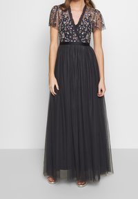 Schwarzes Maxikleid mit taillierter Brust, floralem Stickmuster, transparenten kurzenÄrmeln und einem fließenden Tüllrock. Satiner Bund betont die Taille.