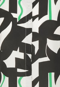 Chemise boutonnée arborant un motif abstrait noir et blanc avec des accents verts, fabriquée dans un tissu lisse avec un léger éclat.
