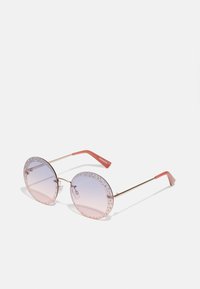 Occhiali da sole tondi con montatura in metallo dorato, lenti rosa chiaro e un design borchiato lungo i bordi. Accenti arancioni sulle astine.