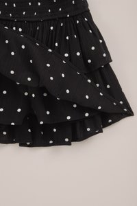 Jupe noire à volants avec des pois blancs, taille élastique froncée, tissu texturé et ourlet à volants superposés.