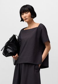 Czarna bluzka o strukturalnej fakturze z kwadratowym dekoltem, krótkimi rękawami i luźnym krojem; zestawiona z czarną, elegancką torebką.