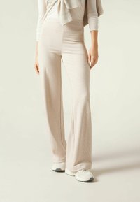 Geribbelde, lichtbeige wijde broek met een hoge taille, gecombineerd met witte sneakers. Glad textuur en vloeiende silhouet.