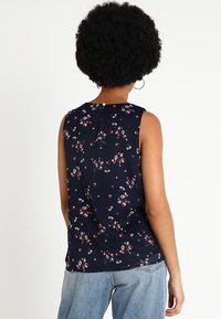 Marinblå ärmlös topp med blommönster, lättviktig tyg, har knäppning bak och en avslappnad passform.