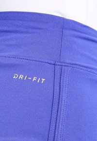 Primer plano de mallas deportivas azules con costuras visibles y logo blanco "DRI-FIT" en la tela.