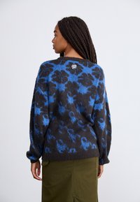 Maglione oversize in tessuto floreale blu e nero, morbido al tatto, con scollatura rotonda, polsini a coste e un patch con logo sul retro.