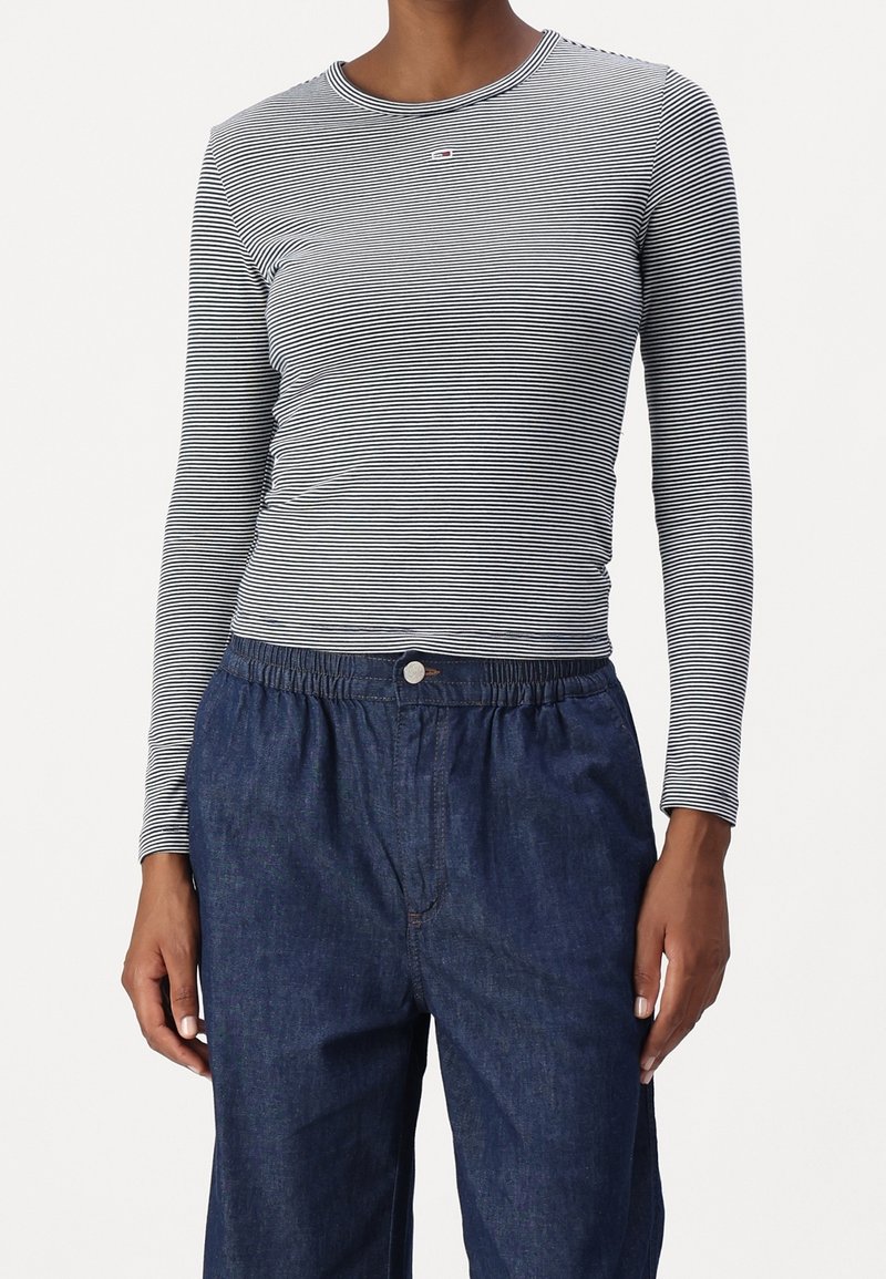 Långärmad randig topp i svart och vitt med rund halsringning, tillsammans med löst sittande mörka jeansbyxor med elastiskt midjeband.