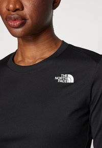 Top a maniche lunghe nero realizzato in tessuto testurizzato, con colletto rotondo e logo The North Face bianco sul lato sinistro del petto.