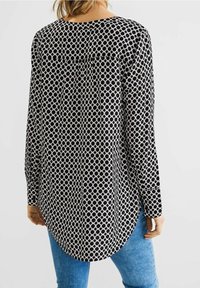 Černobílá halenka s dlouhým rukávem, která má kulatý vzor, kulatý výstřih a zakřivený lem. Vyrobena z lehkého materiálu.
