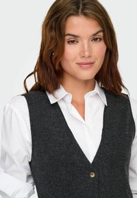 Gilet en laine gris foncé avec un design en V, doté d'une fermeture à un bouton, porté par-dessus une chemise à col blanc. Texture lisse.