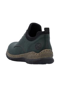 Chaussure slip-on vert foncé avec un col rembourré noir, une semelle intermédiaire texturée beige, une semelle extérieure en caoutchouc noir et un logo circulaire embossé sur le talon.