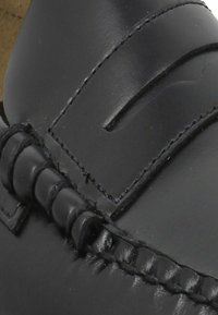 Black leather shoe with a smooth texture, featuring decorative stitching and a slip-on design, emphasizing a streamlined silhouette.