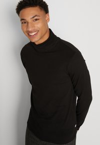 Svart langermet høyhalset genser med en myk tekstur, slim fit og minimalistisk design. Har høy krage og skulderdetaljer.