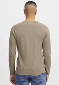 Długi rękaw, oliwkowa ribbed t-shirt z okrągłym dekoltem i rękawami raglanowymi, zestawiony z niebieskimi dżinsami. Posiada małą metkę marki na brzegu.