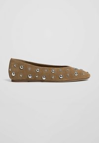 Chaussure plate en daim marron décorée de clous ronds argentés de différentes tailles sur un fond uni.