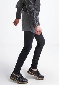 Svart lädermotorjacka med ribbade detaljer, grå t-shirt, åtsittande svarta jeans och blanka svarta skor med spännen och tjocka sulor.