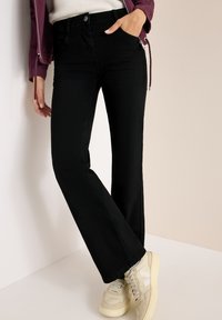 Jeans neri a zampa d'elefante realizzati in denim morbido con tasche anteriori, indossati con sneakers crema dotate di accenti bianchi e un design strutturato.