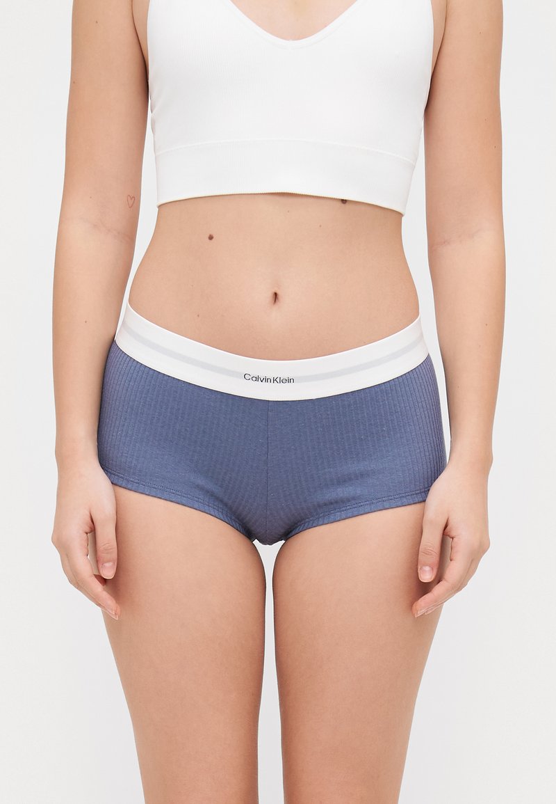 Calvin Klein damesshorts i ribbet navy materiale, med en hvit elastisk midjebånd med logo og to hvite striper.