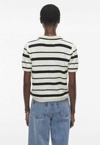 Suéter de punto de manga corta con rayas horizontales en blanco y negro, tejido texturado y escote redondo, combinado con jeans de cintura alta.