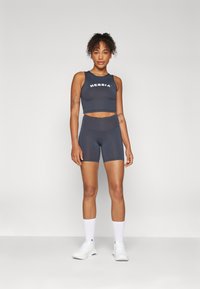 Sivi sportski crop top s bijelim logotipom "NEBBIA", uparen s visokim sivim šortsevima. Model nosi bijele tenisice i čarape do gležnjeva.