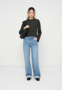 Rebrasti tamnozeleni crop top, svijetloplave traperice s visokim strukom, preklopljene manžete, crna torba i crne cipele. Jednostavan i moderan izgled.