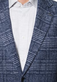 Niebieski żakiet w kratę, wykonany z teksturowanej tkaniny, z klapami, dwiema przednimi kieszeniami oraz zapięciem na pojedynczy guzik, noszony na jasnej koszuli.