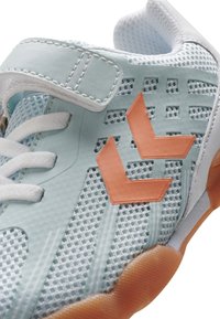 Baskets de sport bleu clair avec tige en maille, lacets blancs, une sangle velcro, et des accents géométriques oranges sur le côté. Semelle en caoutchouc texturé.