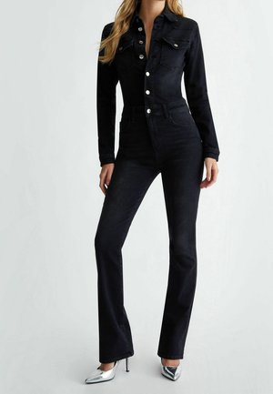 Musta denim-huopa pitkähihaisilla, tiukalla vartalolla, kahdella rintataskulla ja hopeanvärisillä napeilla. Laajenevat lahkeet, joissa on sileä pinta ja klassinen muotoilu.