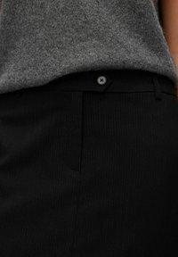 Pantalons à rayures noires avec une texture lisse, dotés d'une fermeture à bouton et de poches latérales, portés avec un haut en laine gris.