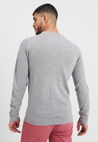 Grå tröja med rund halsringning, långa ärmar och mjuk textur. Baksidan är enfärgad med rak fåll, ihopparad med rosa byxor.