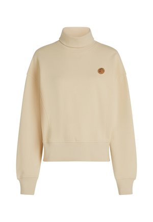 Beige polotröja tillverkad av mjukt tyg, med en avslappnad passform, sänkta axlar och en liten rund logotyp på bröstet.
