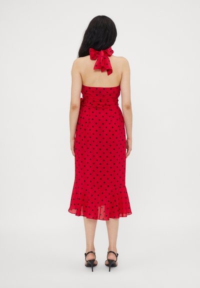 Rochie roșie cu buline albe, cu guler halter și detaliu cu fundiță la spate, având un corset ajustat, tiv evazat și un textil transparent.