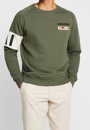 Sweatshirt vert olive à manches longues, avec des poignets côtelés et un col rond. Présente une bande blanche sur le bras, des patches et un tissu texturé.
