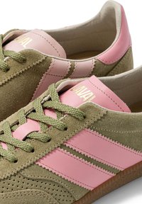 Paire de baskets en daim vert et cuir rose avec des lacets verts et le nom de la marque en or sur la languette et la bride de talon roses.