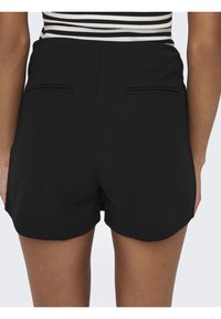 Zwarte shorts met een aansluitend ontwerp, voorzien van twee achterzakken en een gladde textuur. De zoom is licht gebogen voor een getailleerde uitstraling.