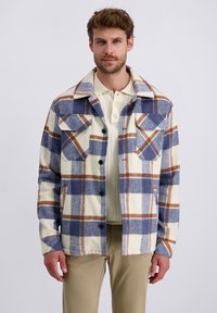 Karierte Flanelljacke in Creme-, Blau- und Brauntönen. Verfügt über große Brusttaschen, Knopfleiste und eine weiche Textur.