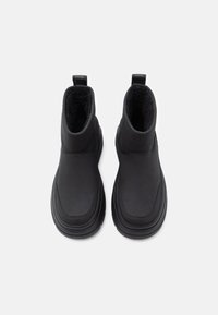 Černé kotníkové boty s hladkým syntetickým svrškem, měkkou vnitřní podšívkou a gumovou podrážkou. Vybavené poutky pro snadné obouvání a minimalistickým designem.