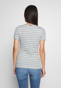 Camiseta a rayas grises con mangas cortas, diseño entallado y una pequeña etiqueta de color en la parte posterior del cuello. Combinada con unos vaqueros azules.