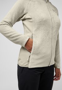 Fleece-voering ritsjas in lichtbeige met een gladde stofpaneel. Voorzien van een hoge kraag, zijzakken en een comfortabele pasvorm.